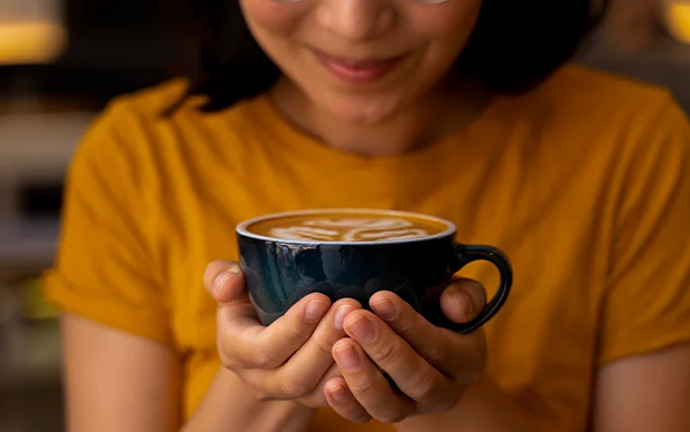 Mulher contente segurando uma xícara de café mostrando o que é café macchiato
