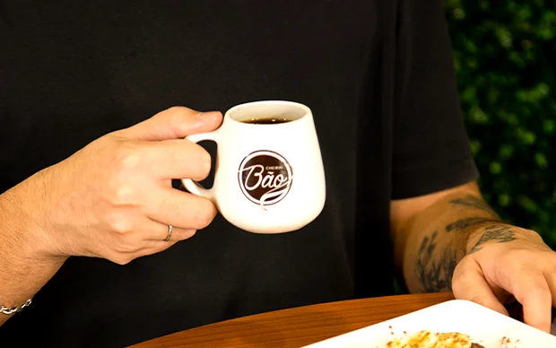 Mulher contente sentada na mesa com uma xícara de café para representar os efeitos da cafeína no cérebro